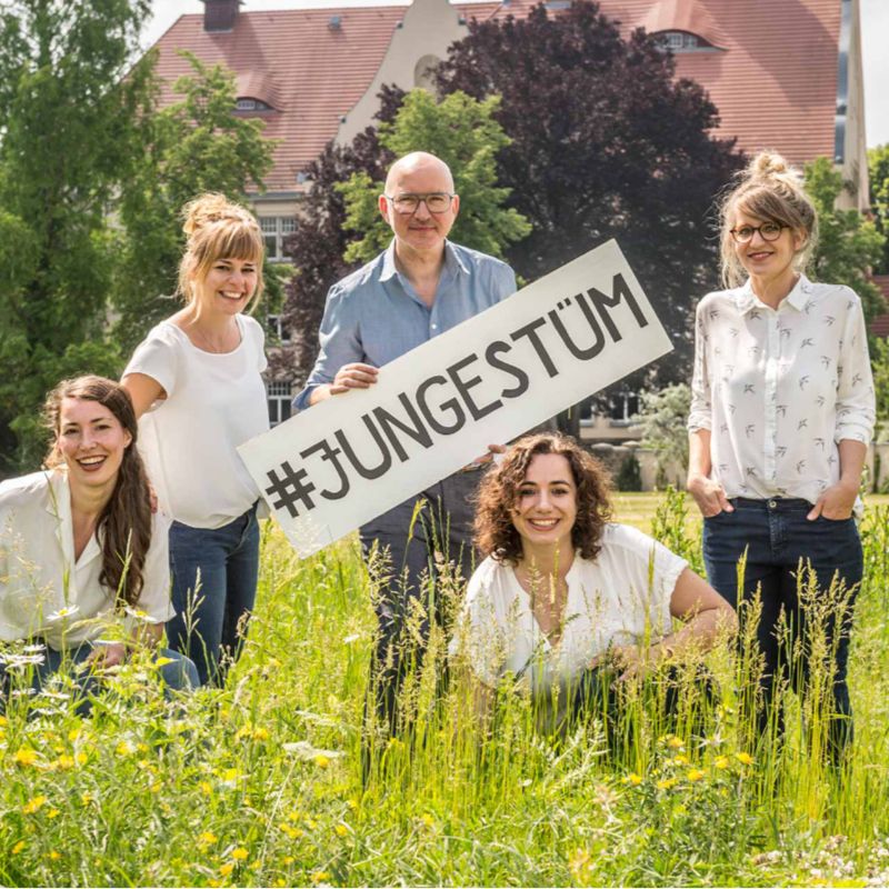 Das Team des junges.studio mit einem Schild auf einer sommerlichen Wiese