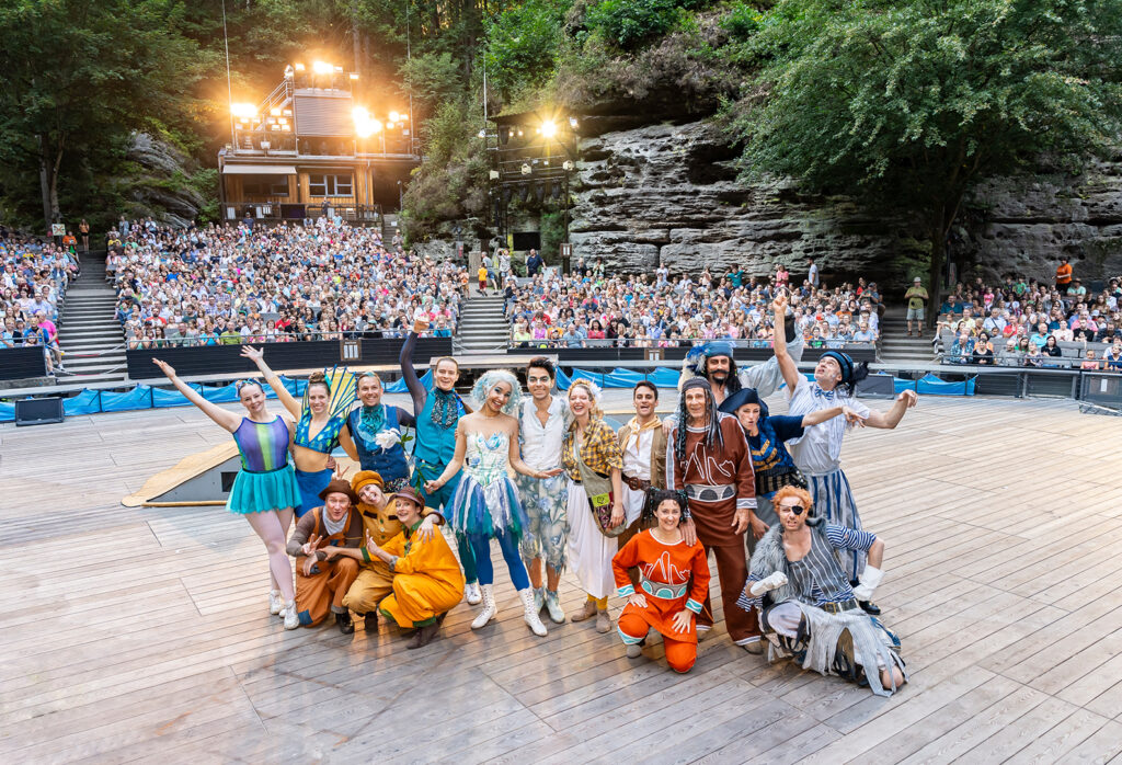 Die Besetzung des Familienstücks Peter Pan steht jubelnd auf der Felsenbühne Rathen. Im Hintergrund ist ein voller Zuschauerraum zu sehen.